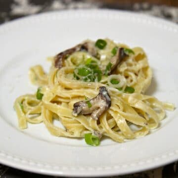 mushroom alfredo and green onions on a white plate