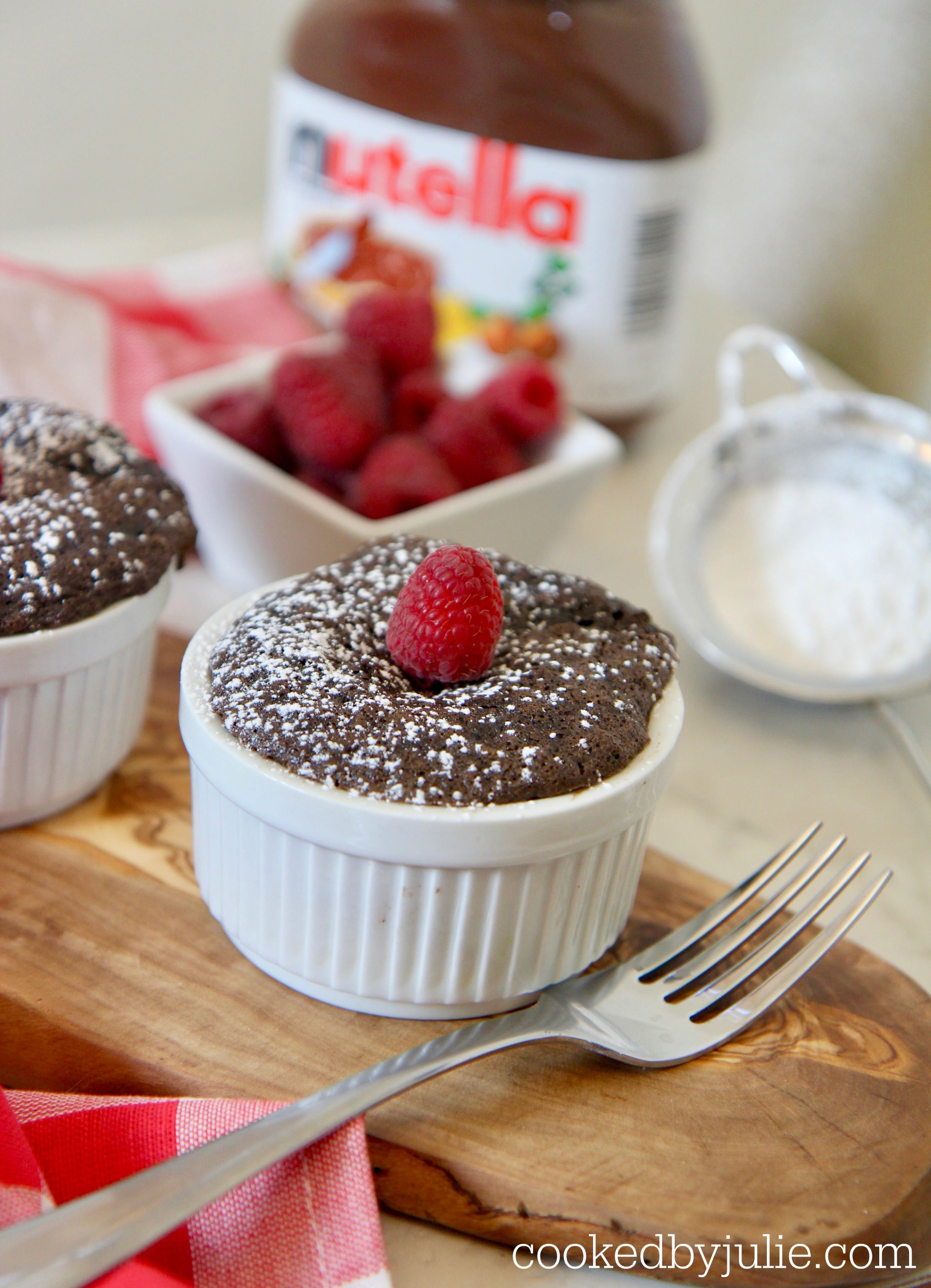 chocolate Nutella cake in a ramekin with powdered sugar and fresh raspberries. 