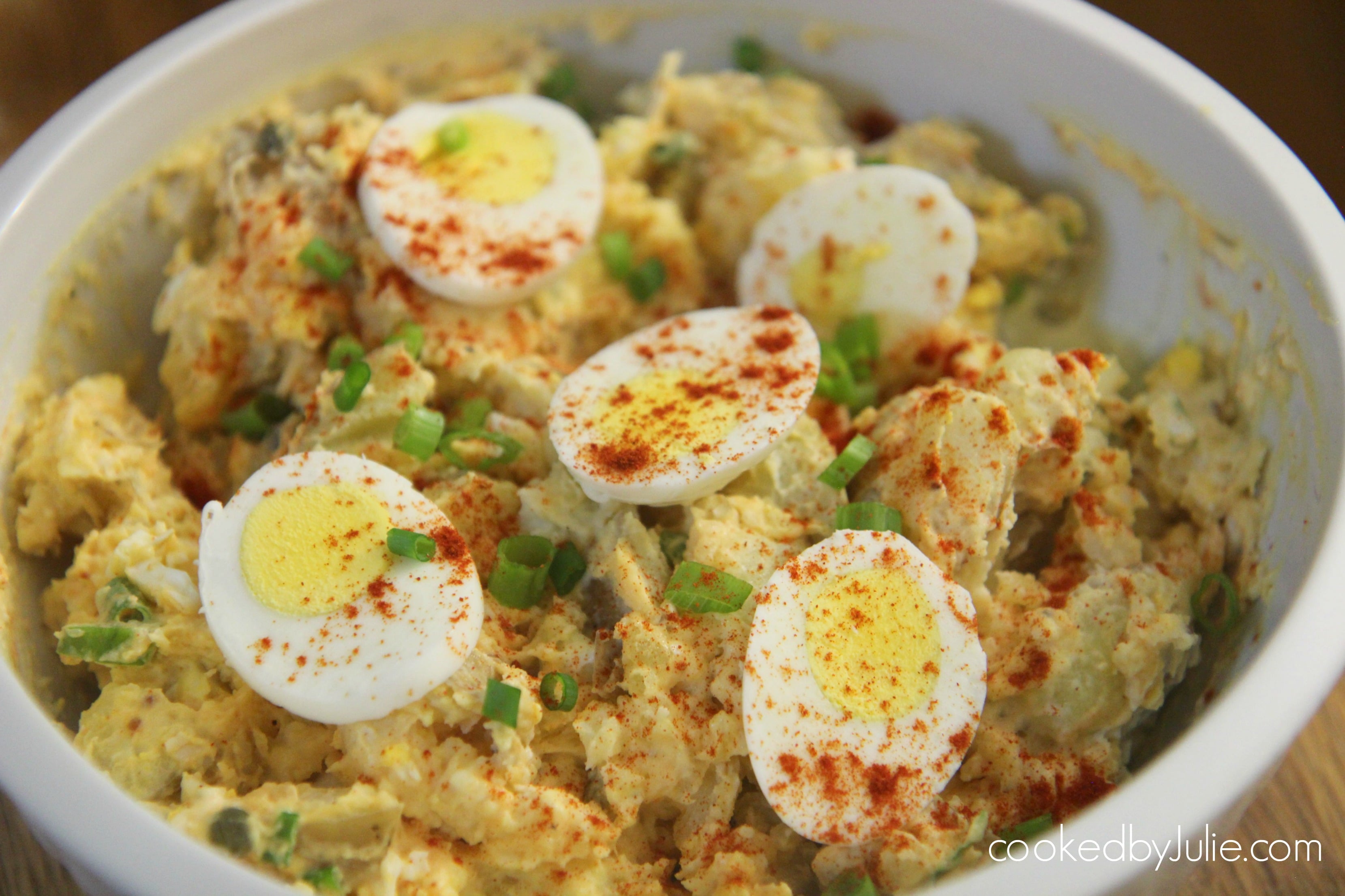 potato and egg salad in a white bowl with 5 eggs on top, paprika, and scallions.