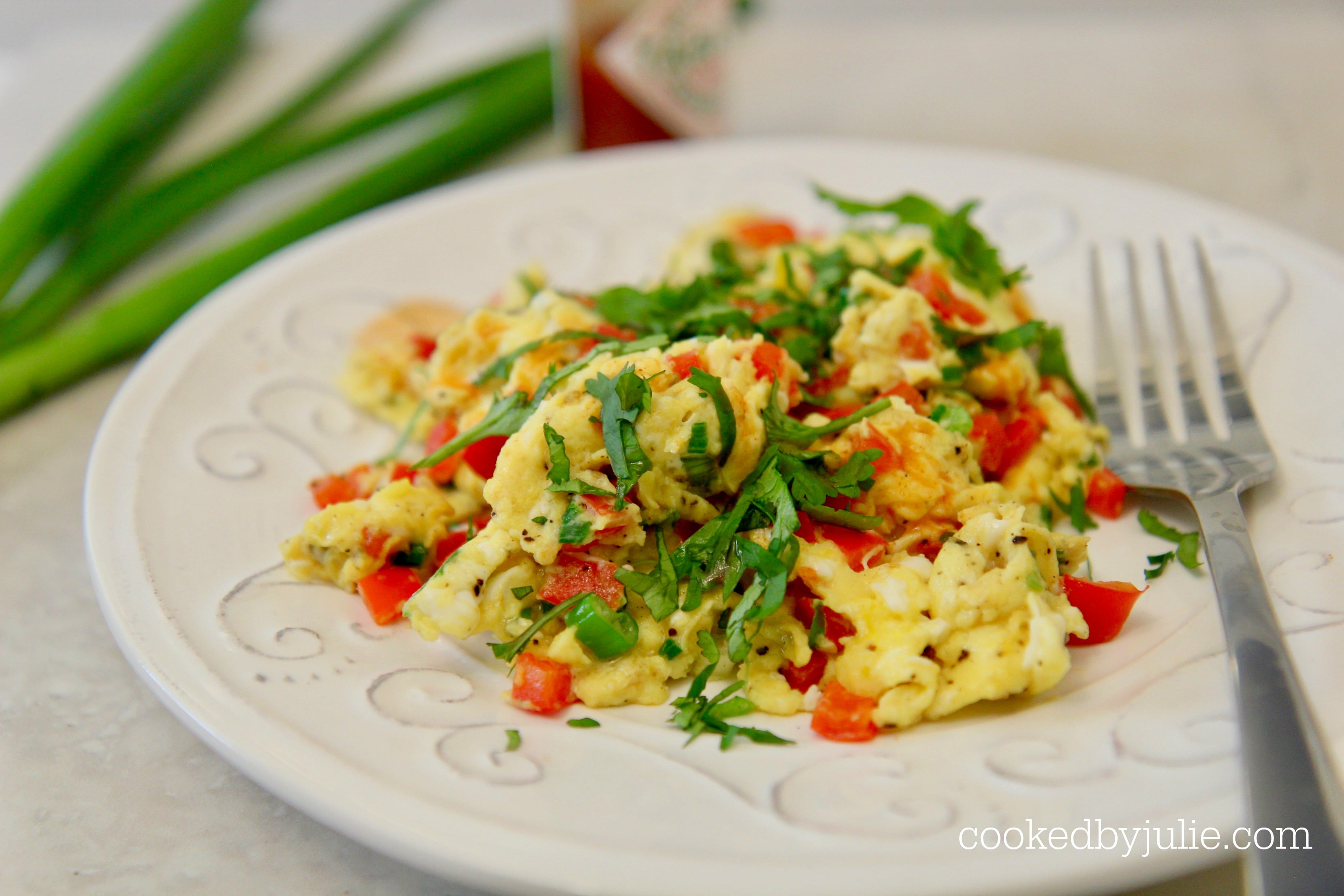 scrambled eggs, scallions, hot sauce, peppers, and cilantro on a white plate. 