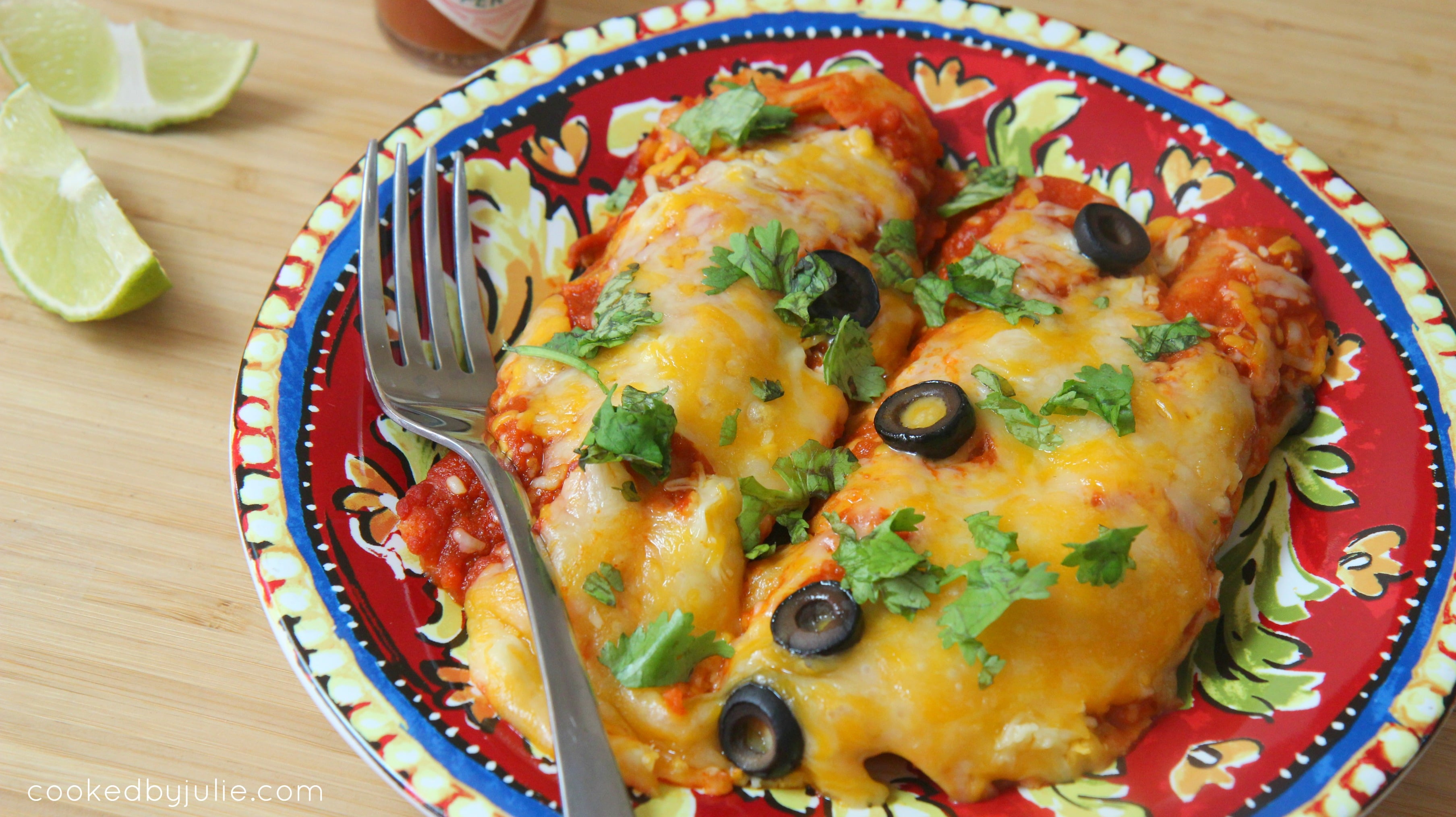 Beef enchiladas served with lime slices, cilantro and sliced black olives