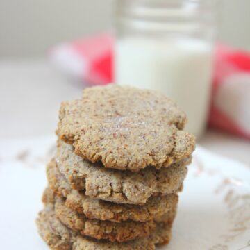 keto sugar cookies on a small white plate with a glass of milk in the background and a white and red towel.