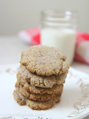 keto sugar cookies on a small white plate with a glass of milk in the background and a white and red towel.