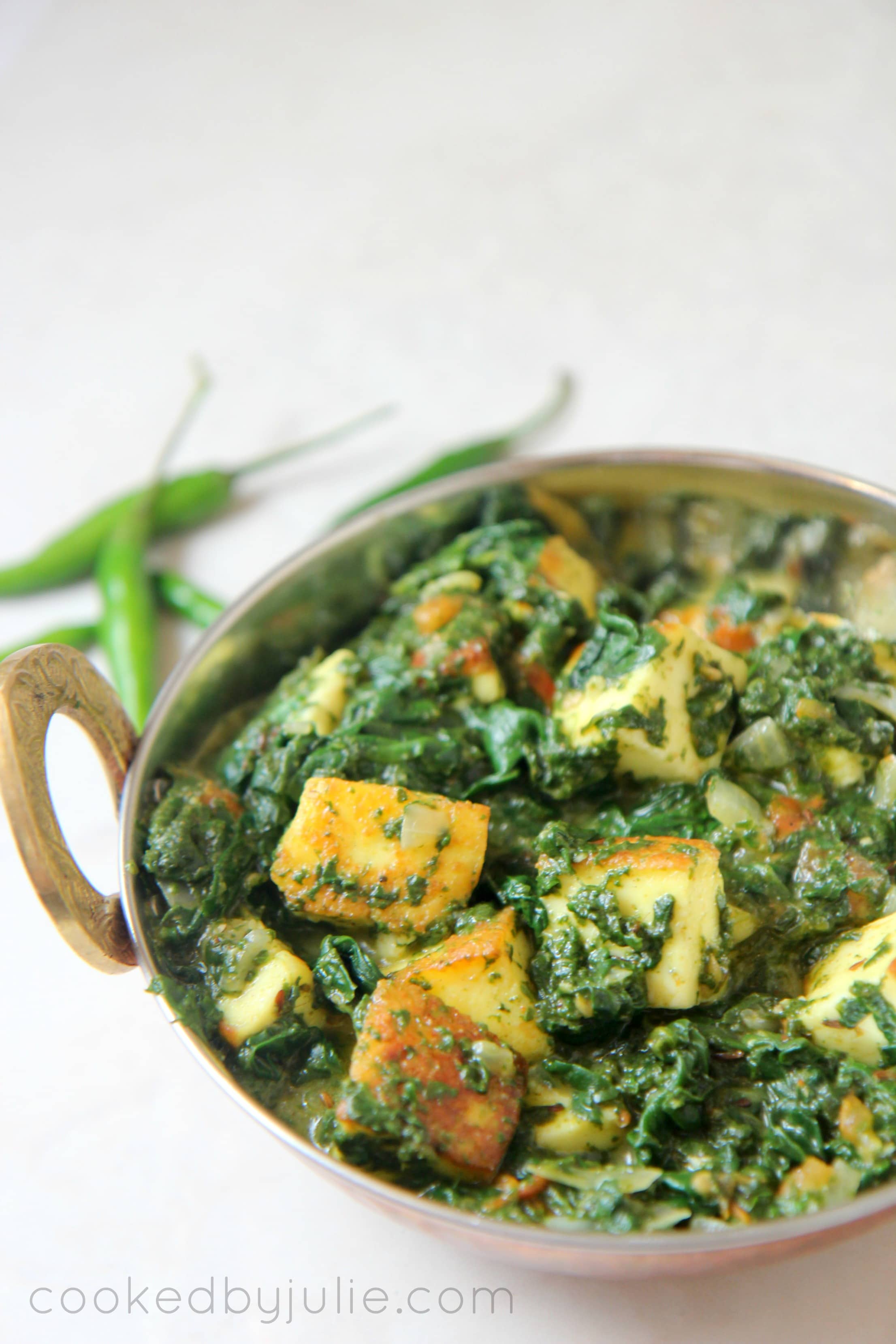 Saag paneer in a gold small dish with green chilies on the side