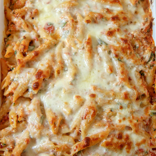 baked ziti with spinach and melted mozzarella cheese on top in a white casserole dish.
