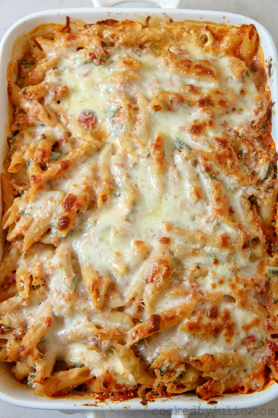 baked ziti with spinach and melted mozzarella cheese on top in a white casserole dish. 