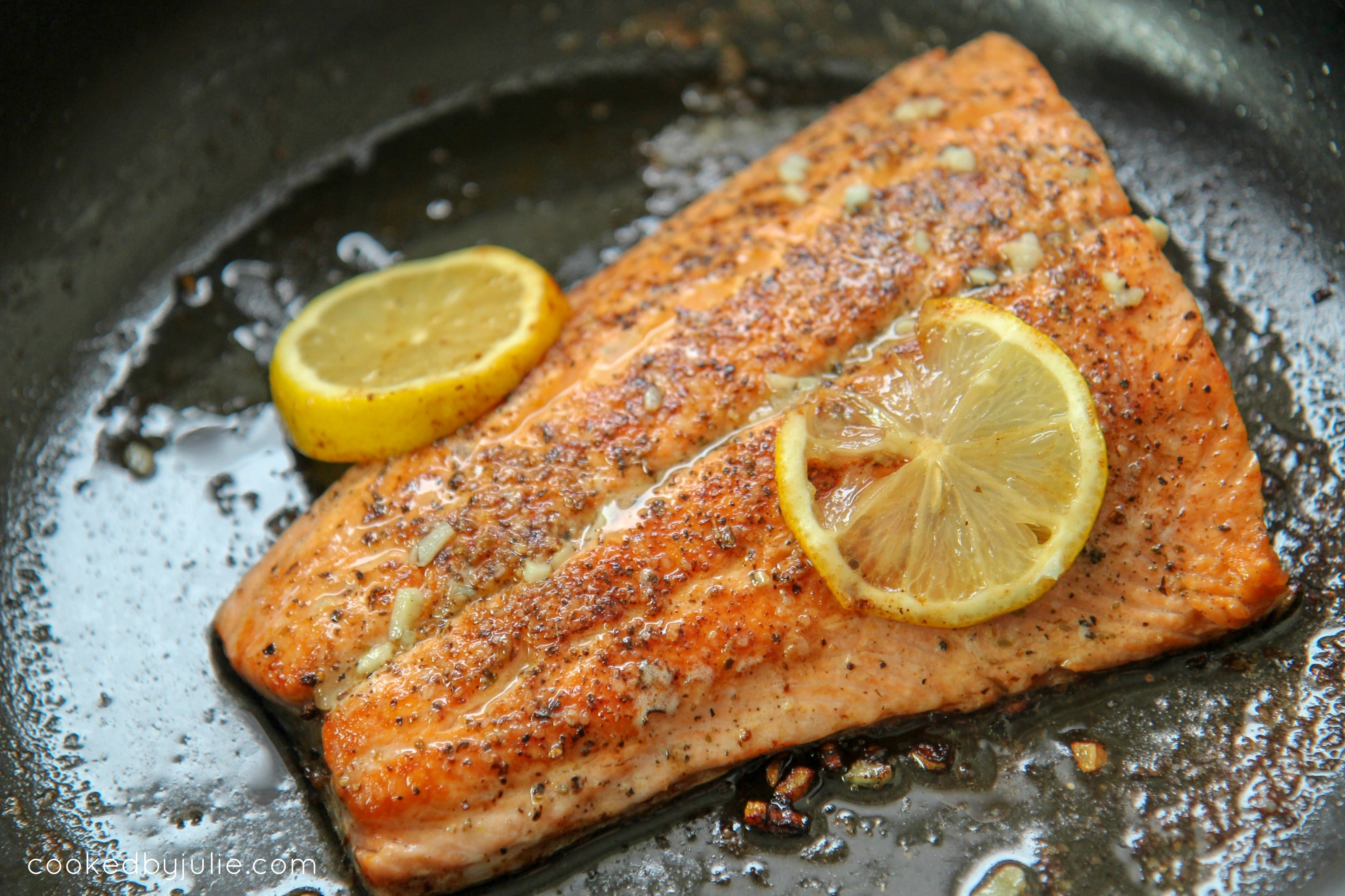 salmon filet in a large skillet with lemon slices 