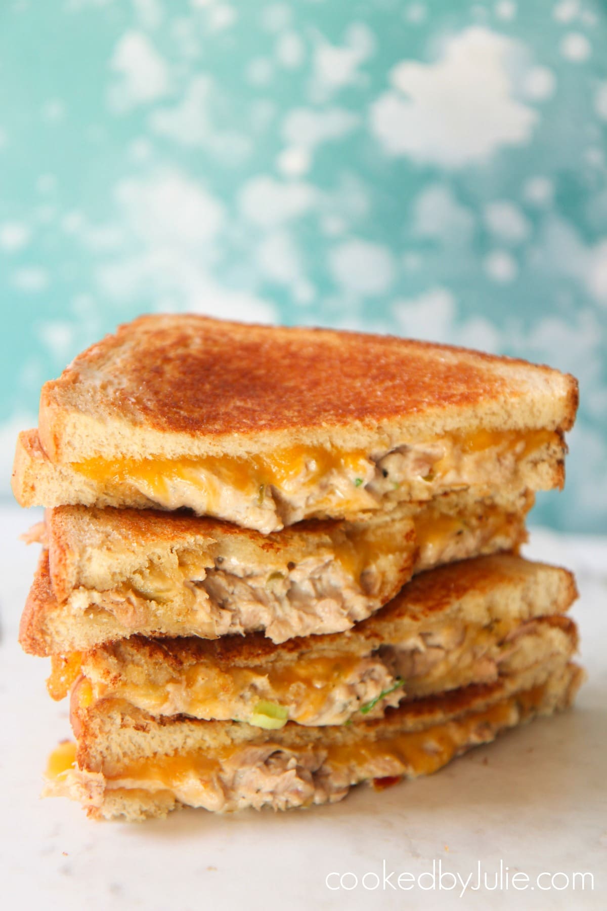 Four tuna melt sandwiches on a white surface with a baby blue and white backdrop. 
