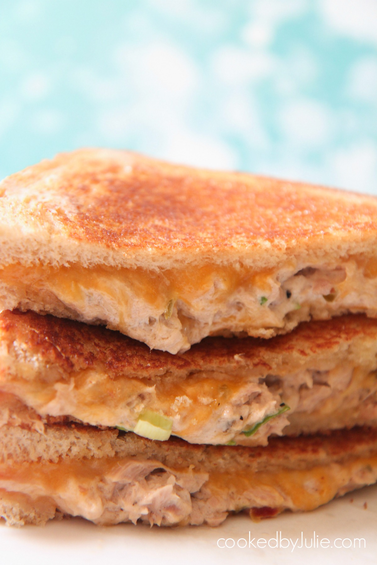 Three tuna melt sandwiches up close with a blue backdrop. 