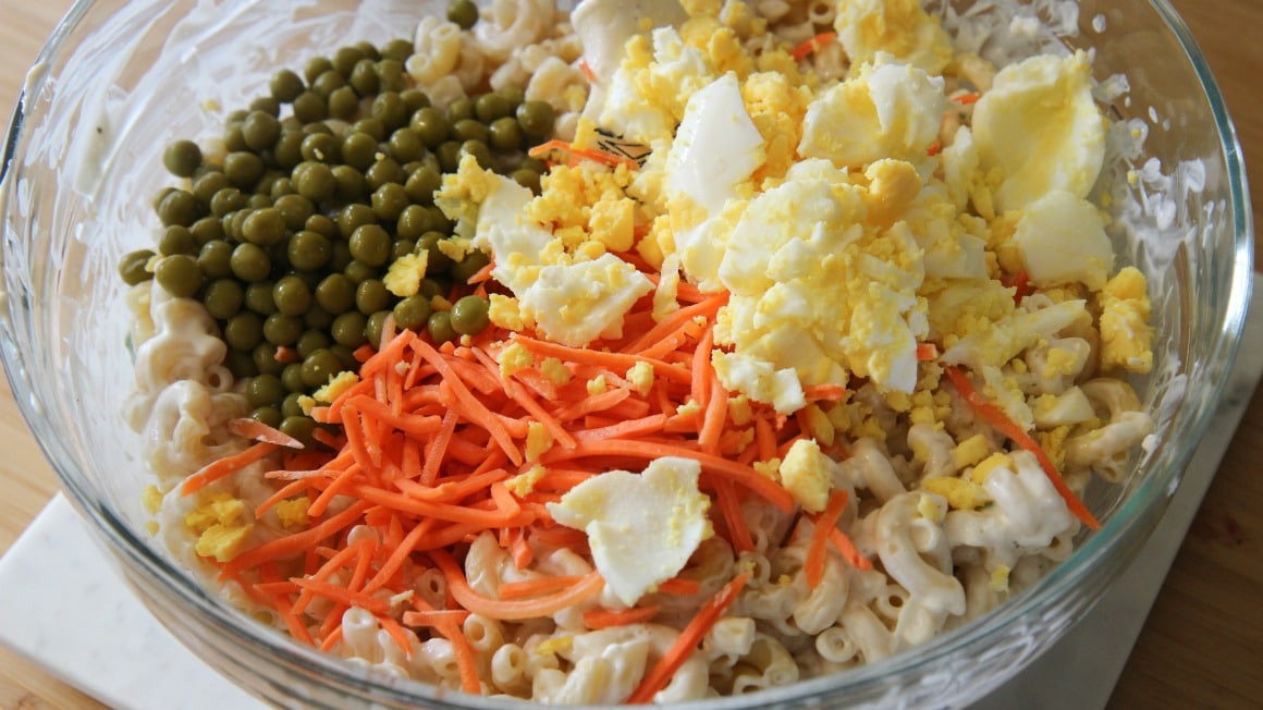 Bowl of Hawaiian Macaroni Salad Ingredients. Green peas, shredded carrots, eggs, and macaroni. 