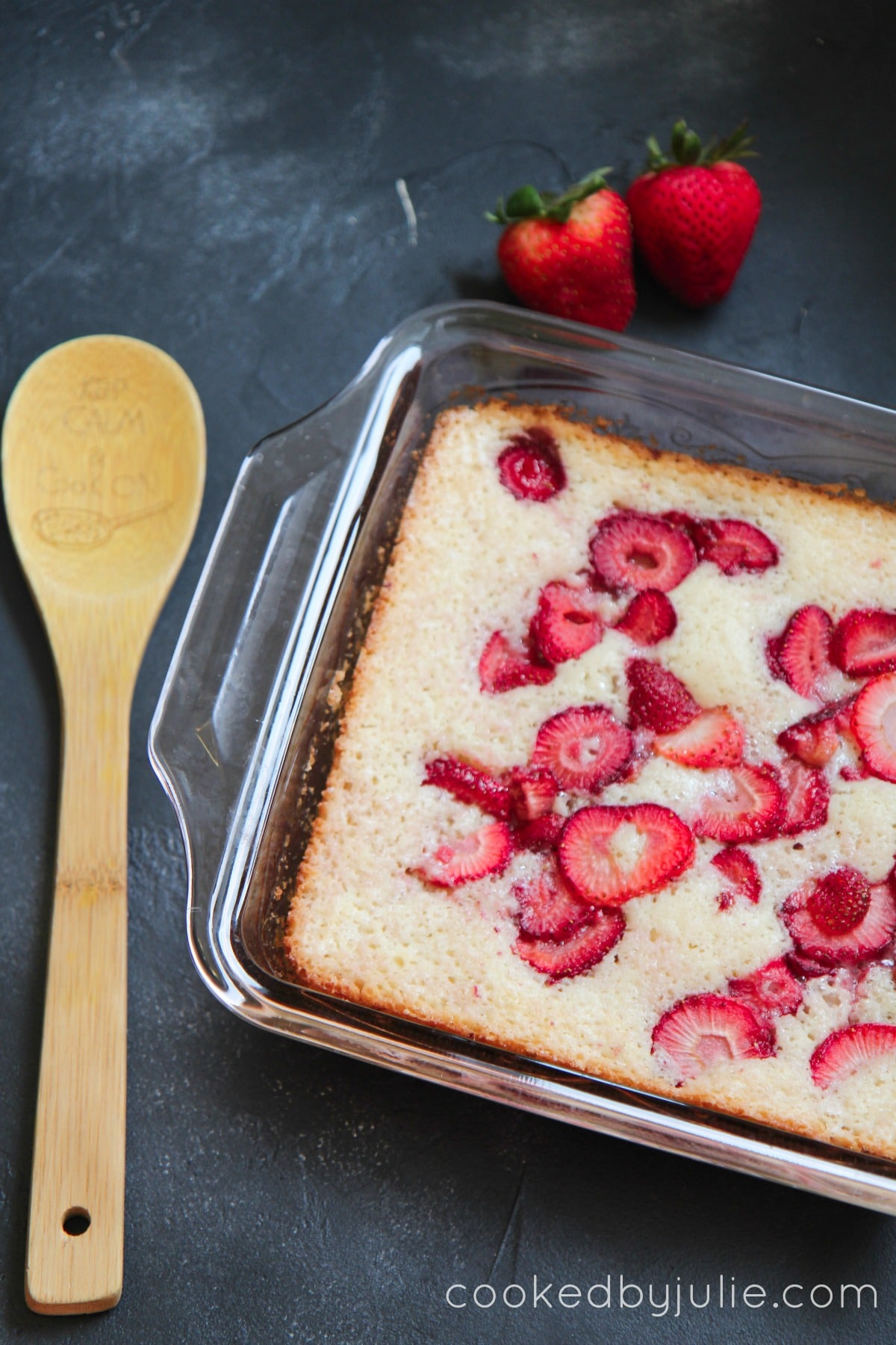 Fresh Strawberry Cobbler in a baking dish with a wooden spoon and two strawberries on the side. 