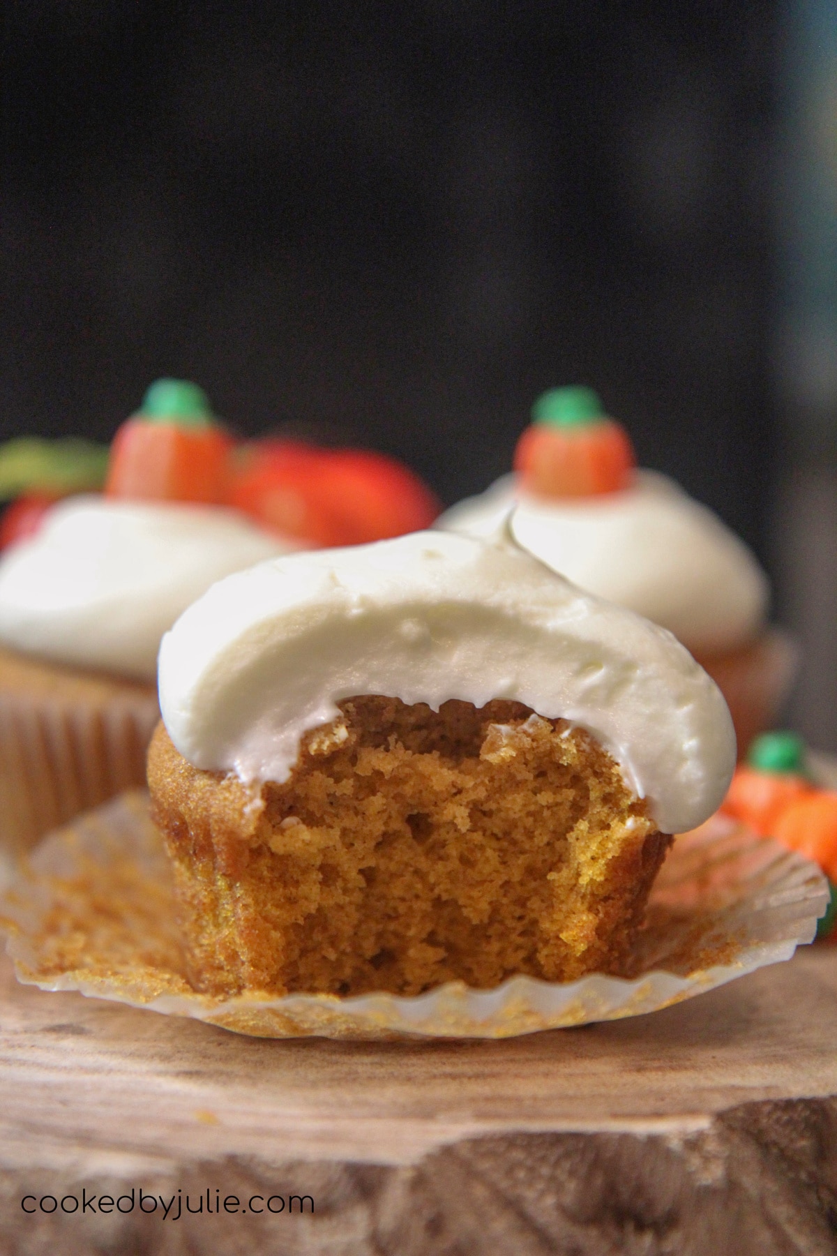 a pumpkin cupcake sliced in half on top of a wooden board with two pumpkin cupcakes in the background. 