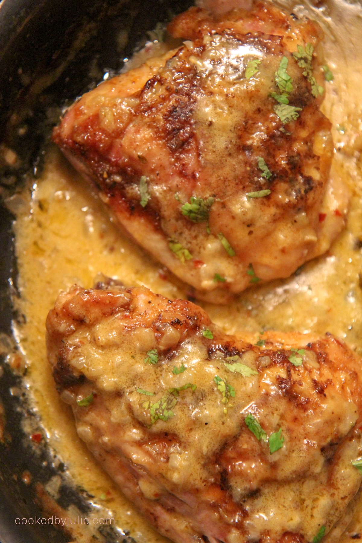 two chicken thighs with cream in a black skillet 