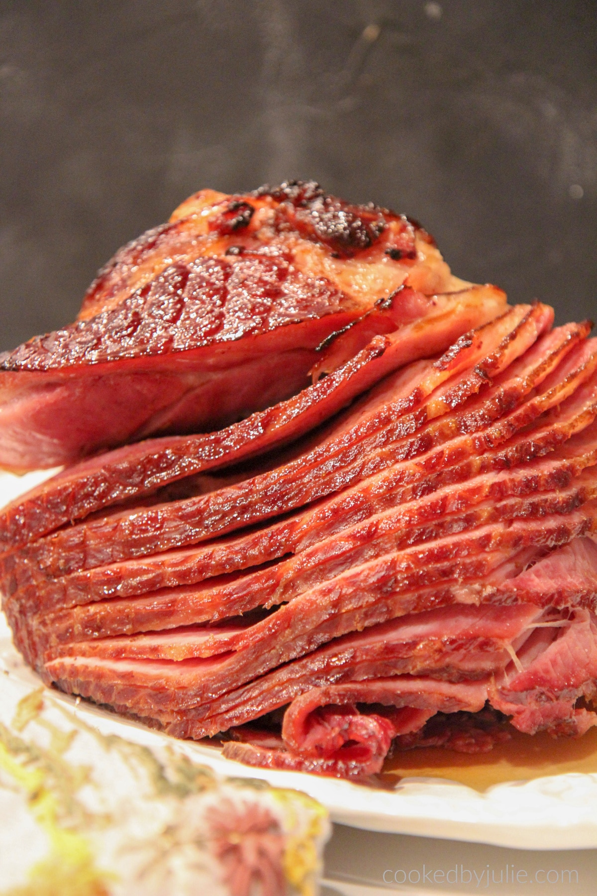 A baked ham with brown sugar glaze on a platter with a dark backdrop. 