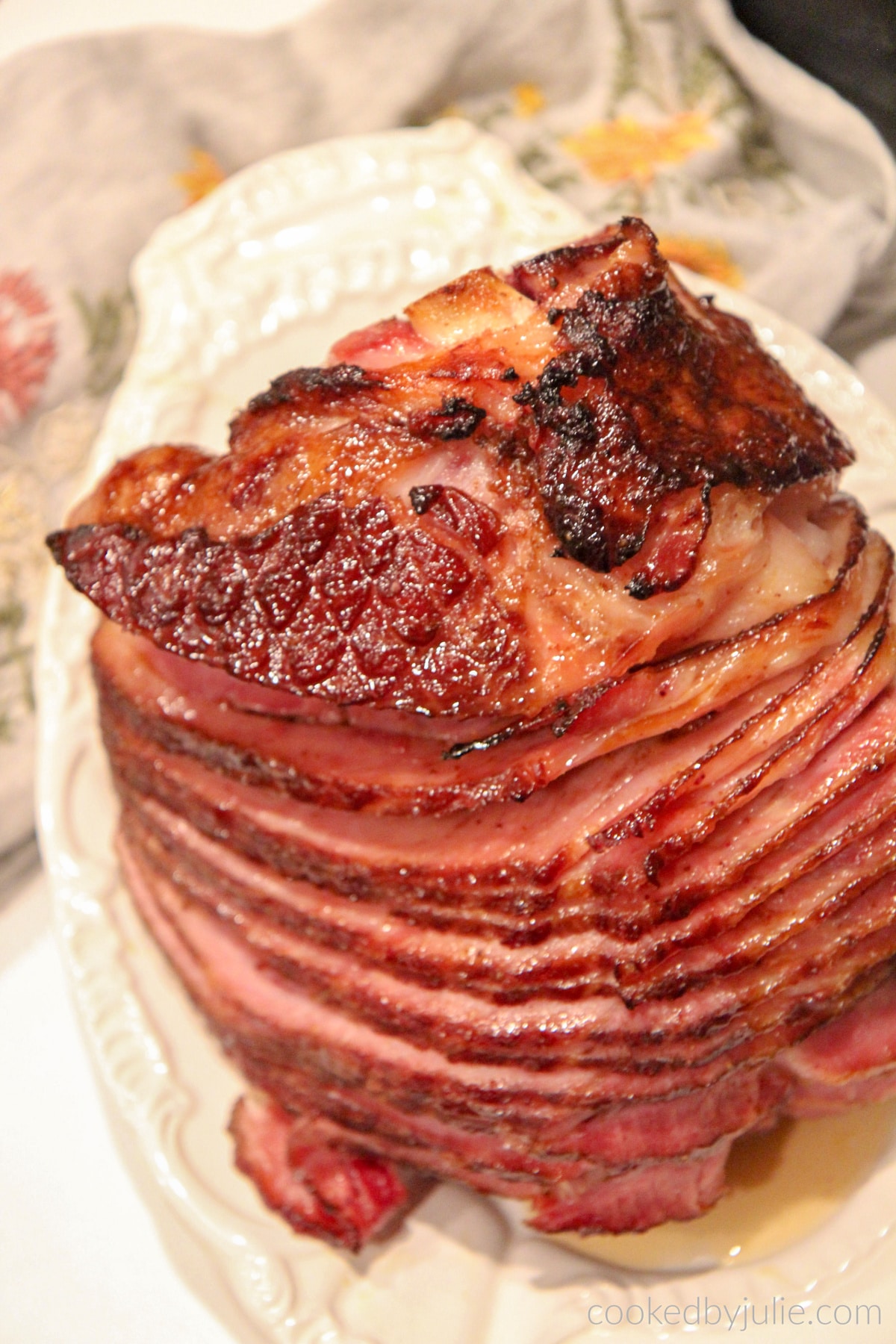 An entire baked ham on a white serving platter with a gray towel on the side. 