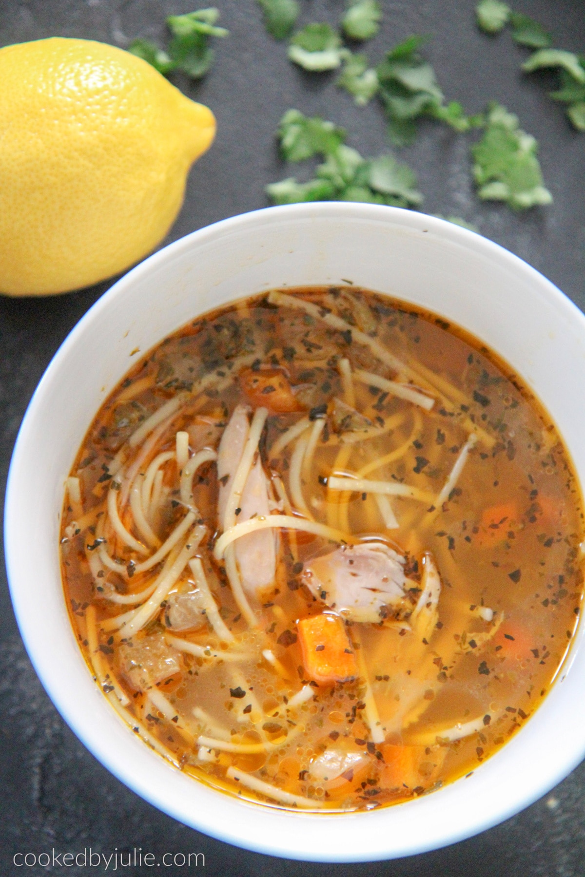 chicken noodle soup in a white bowl with a lemon and parsley on the side. 