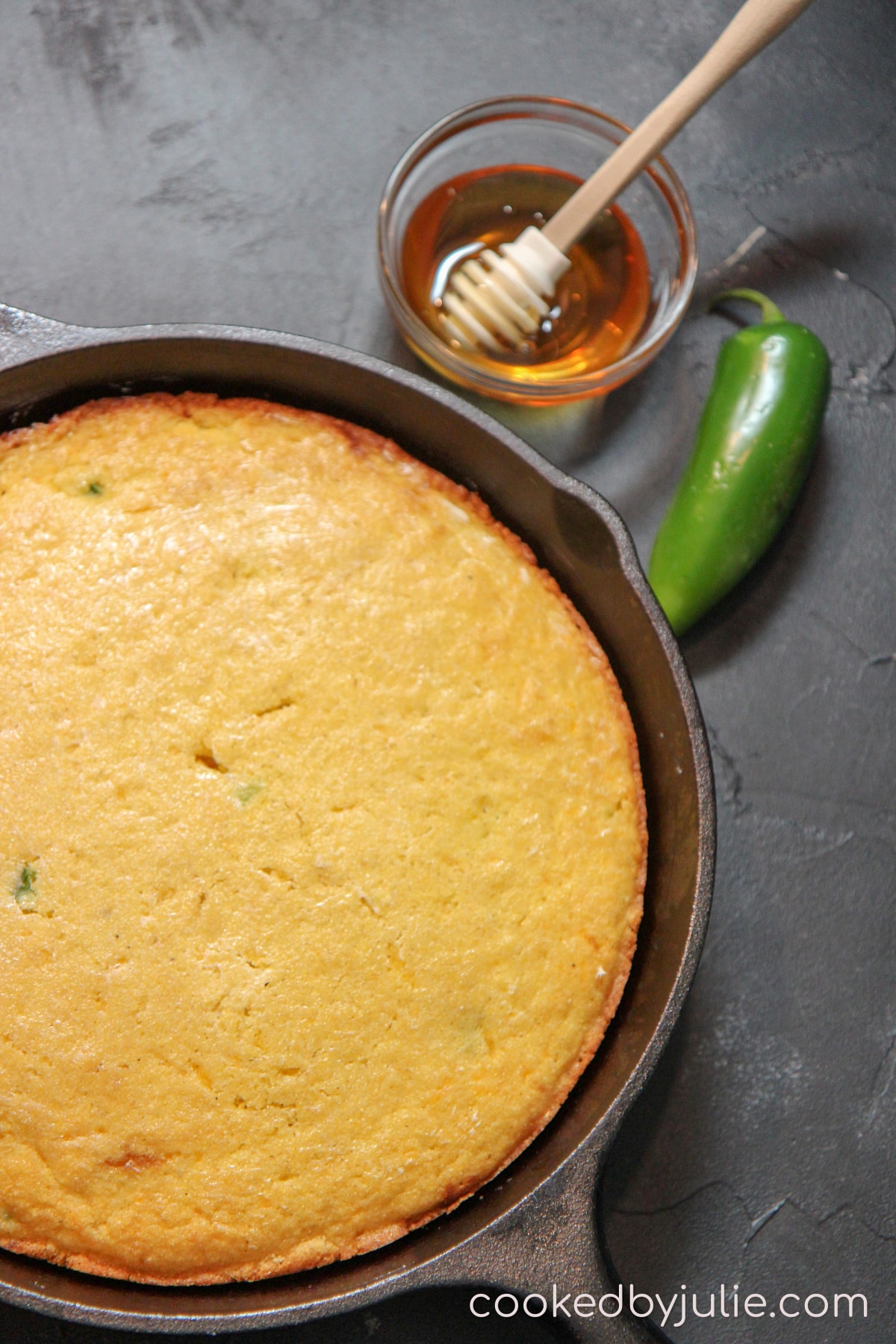 a cast iron skillet with cornbread and a honey comb and small bowl with syrup. A jalapeno pepper in the background. 