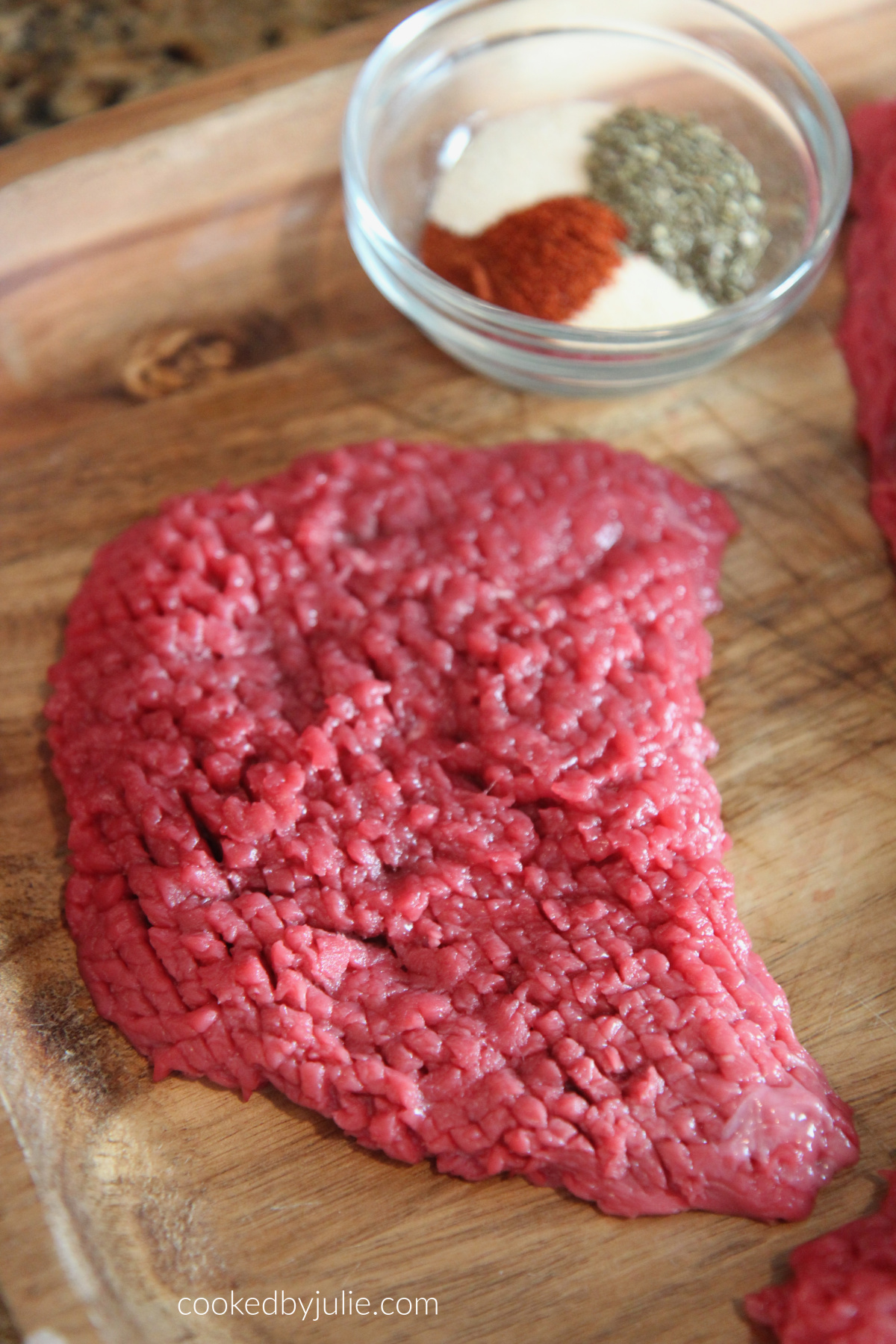 Raw beef steak on a cutting board with a small bowl of spices on the side. 