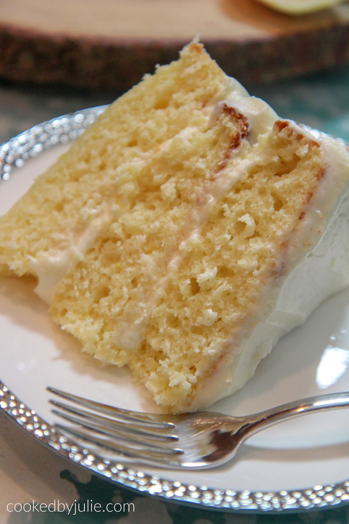a three layer lemon cake slice on a white and sliver plate with a fork on the side. 