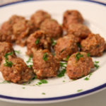 a white and blue plate of turkey meatballs with fresh parsley