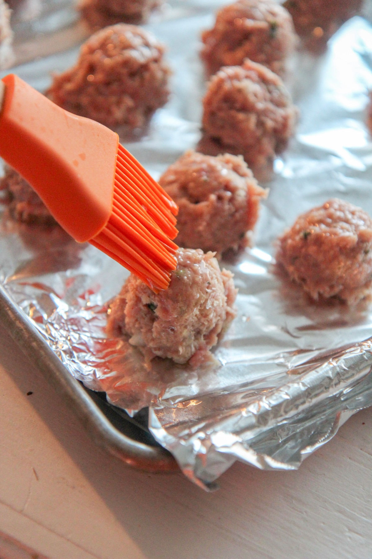 an orange brush and turkey meatballs on a baking sheet 