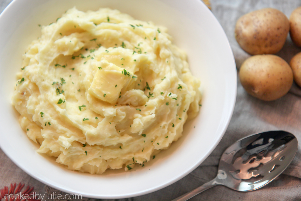 mashed potatoes in a white bowl with a spoon and raw potatoes on the side 