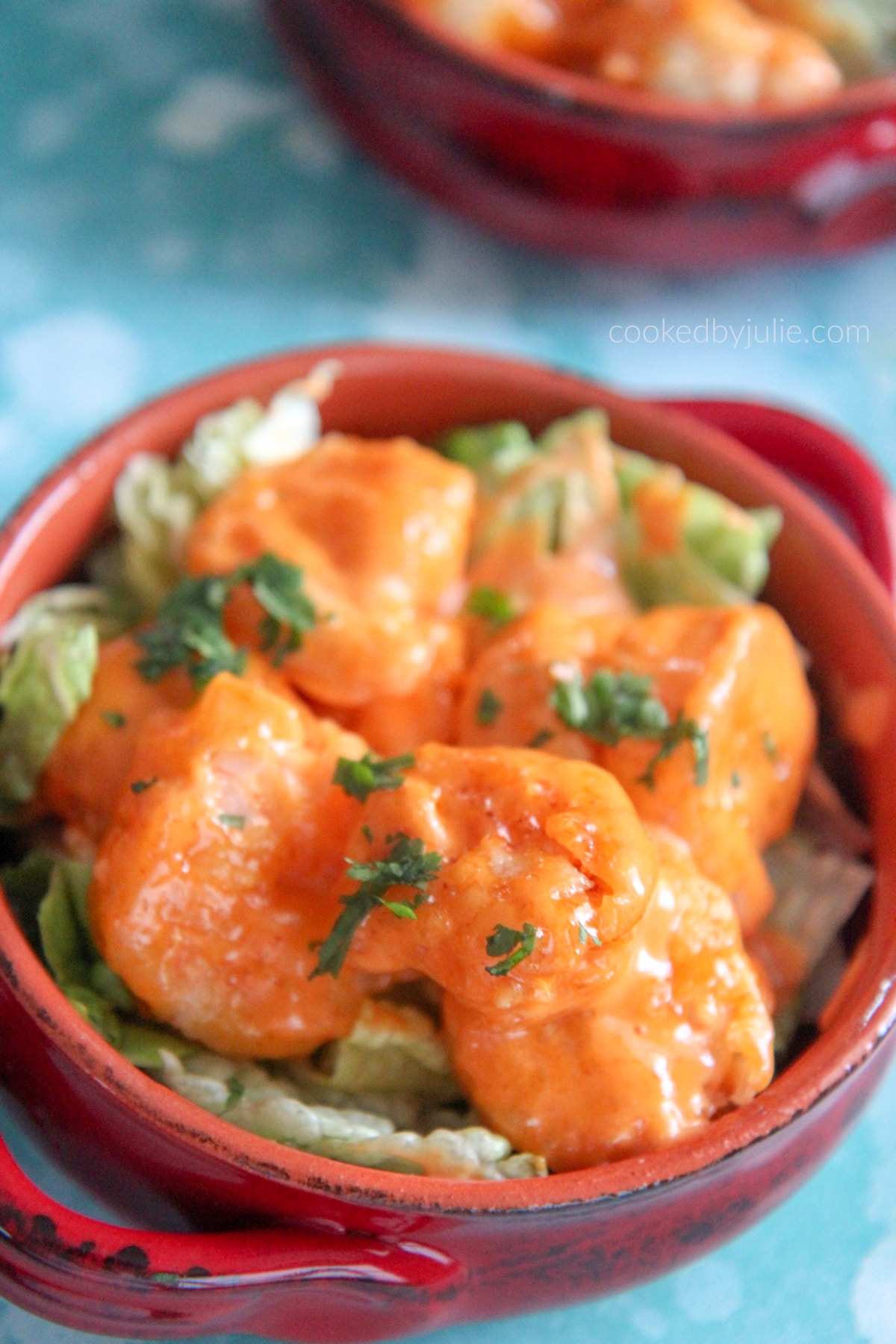 bang bang shrimp on top of lettuce in a red bowl. 