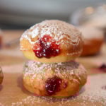 jelly donuts with powdered sugar stacked on top of a wooden board