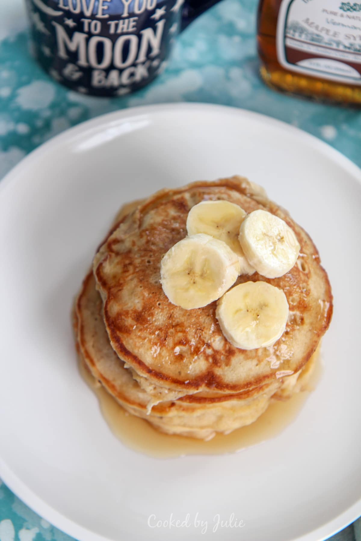 a stack of banana pancakes on a white plate with banana slices and maple syrup