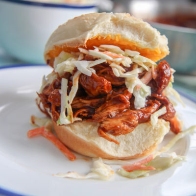 bbq pulled chicken sandwich on top of a white plate with pieces of coleslaw on the plate