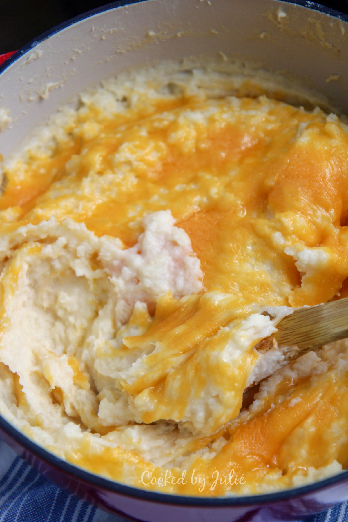 cheddar garlic mashed potatoes in a red dutch oven and wooden spoon