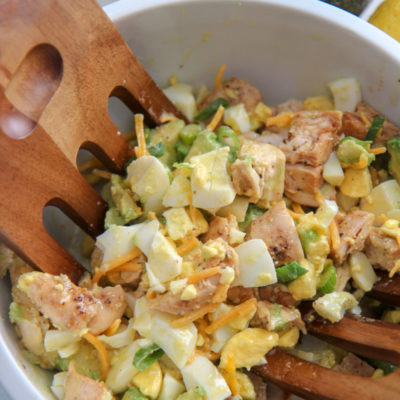 avocado chicken salad in a white bowl and wooden salad mixers