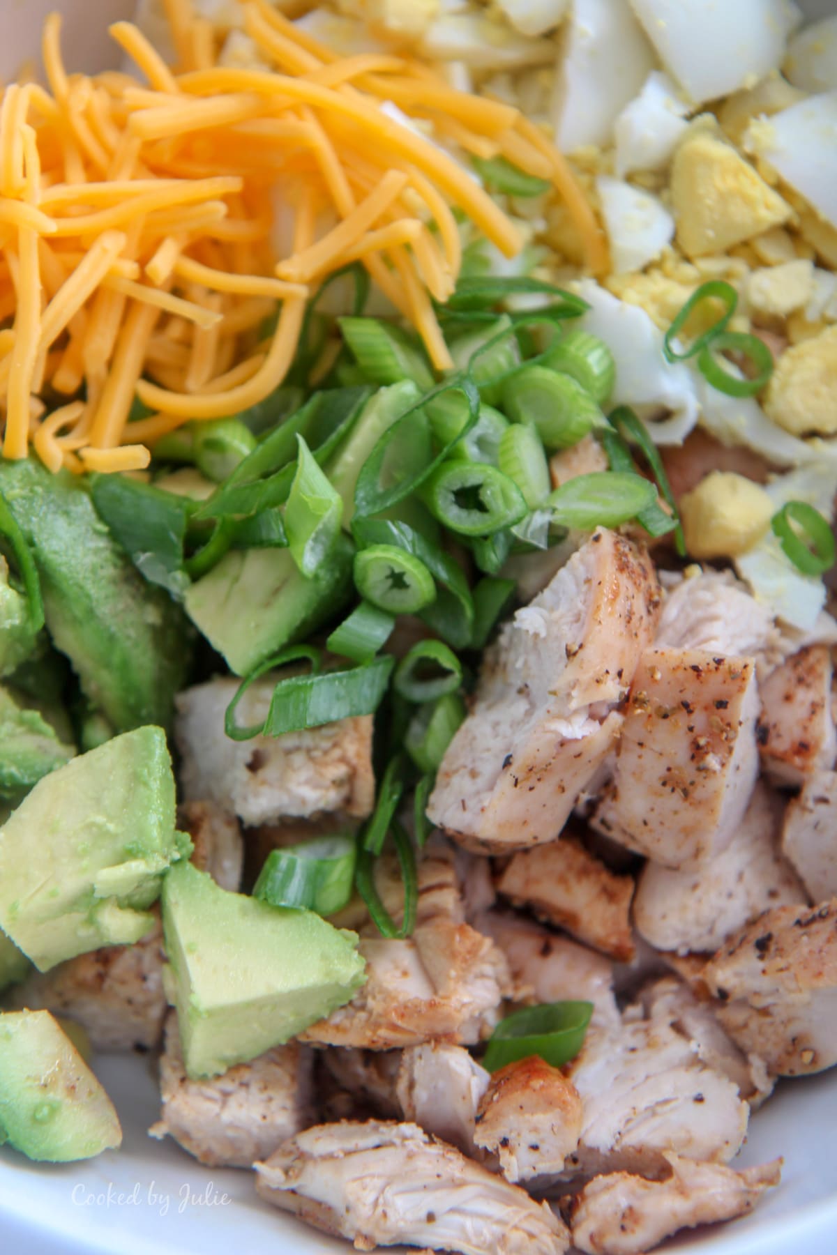 baked chicken, avocados, scallions, cheddar cheese, and boiled eggs in a white bowl