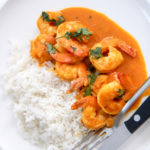 coconut shrimp curry with white basmati rice on a white plate with utensils