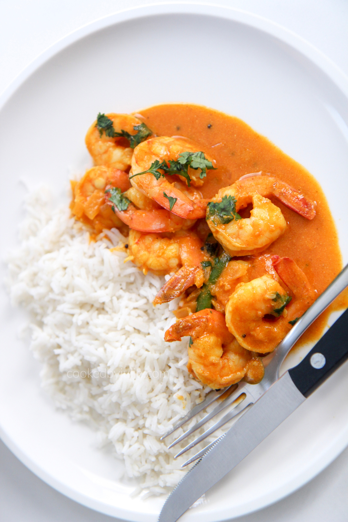 coconut shrimp curry with white basmati rice on a white plate with utensils 