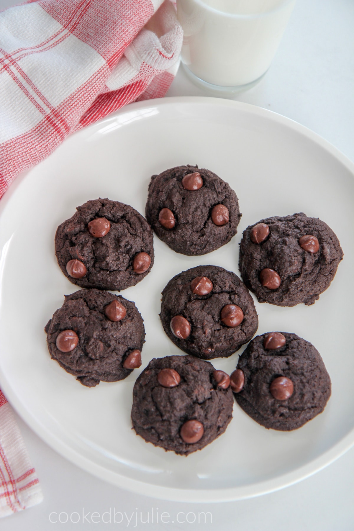 double chocolate cookies on a white plate with a glass of milk and a red and white towel