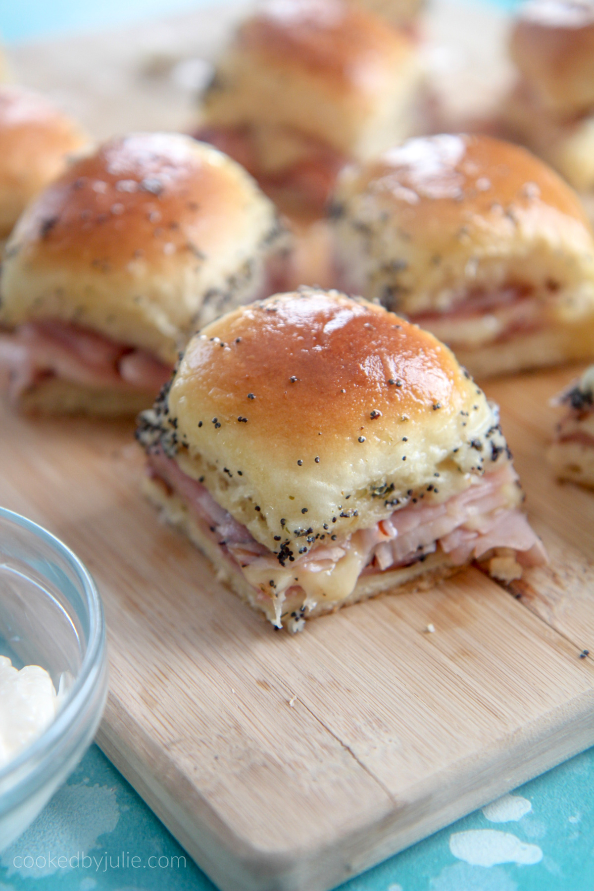 ham and cheese sliders on a wooden board with mayo on the side 