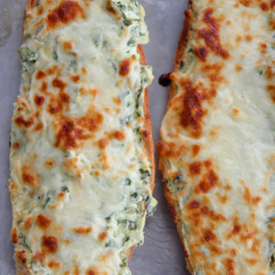two loafs of cheesy spinach artichoke bread on a baking sheet