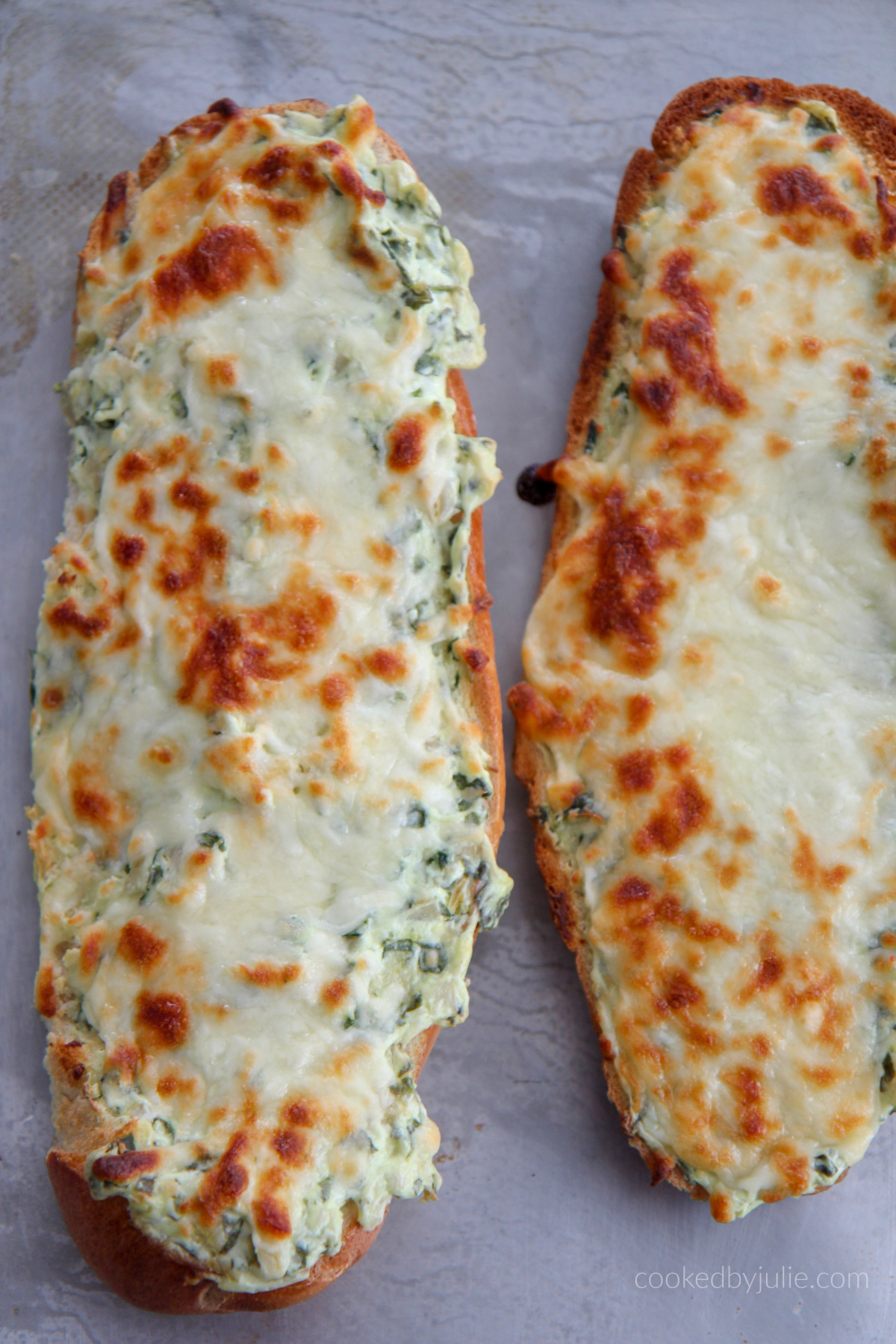 two loafs of cheesy spinach artichoke bread on a baking sheet