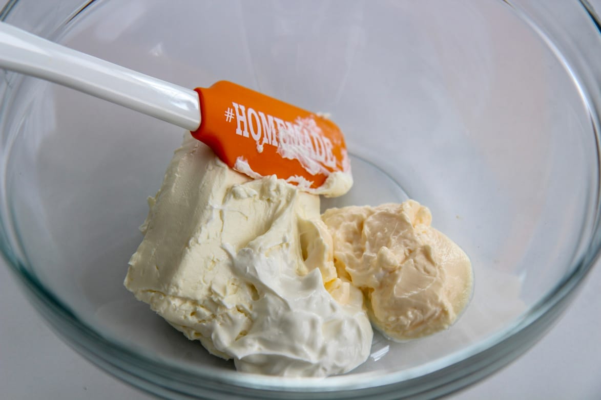 mayo, sour cream, and softened cream cheese in a glass bowl with an orange spatula 