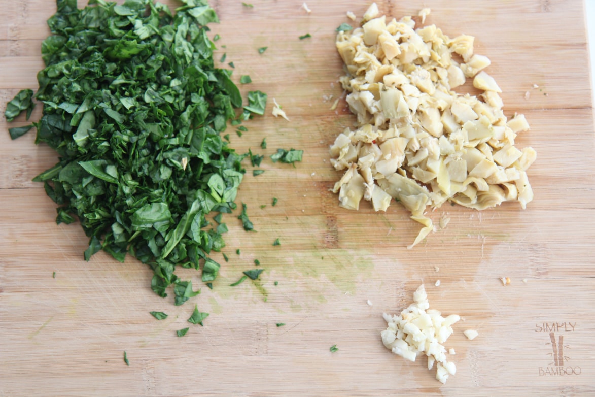 fresh spinach, minced garlic, and roughly chopped artichokes on a wooden board