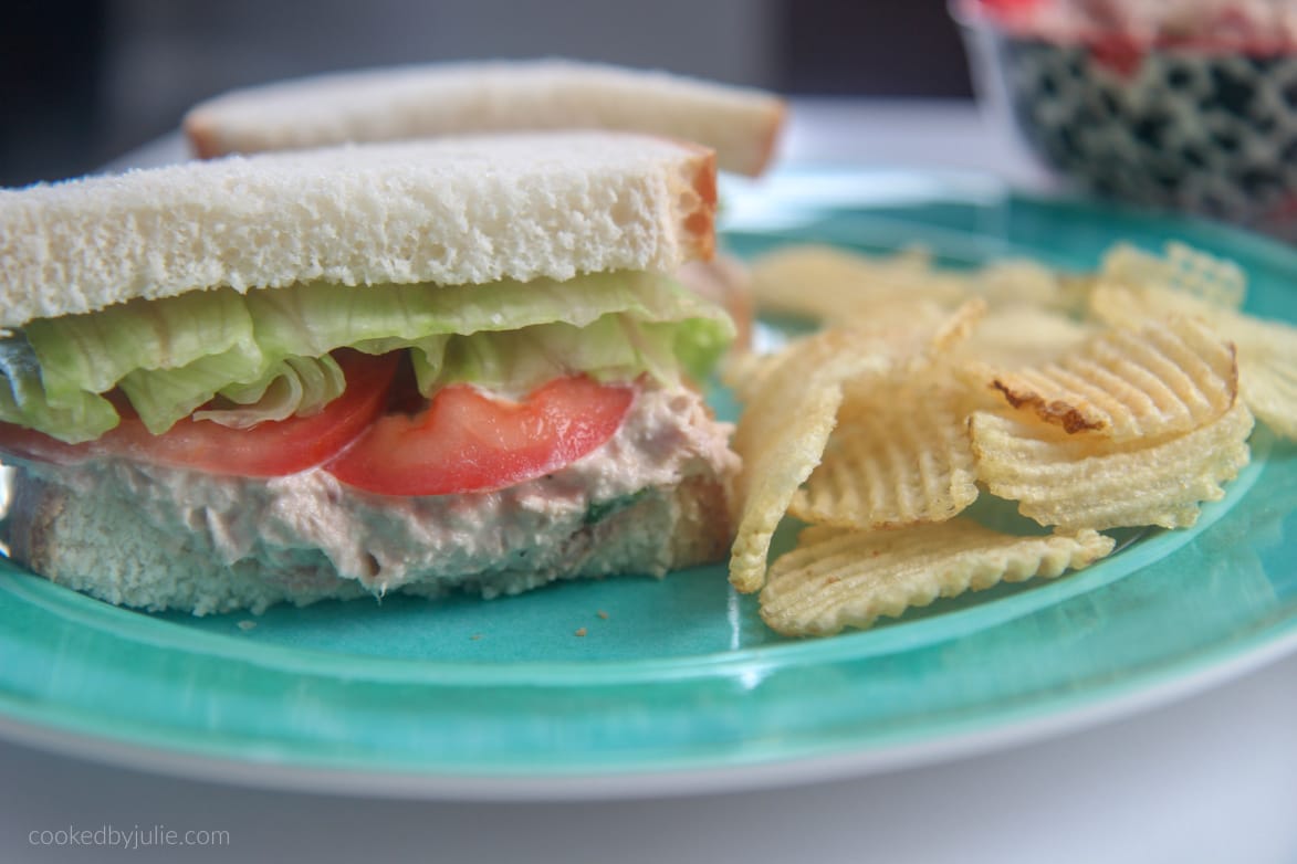 tuna salad sandwich with lettuce and tomato on a blue plate with potato chips 