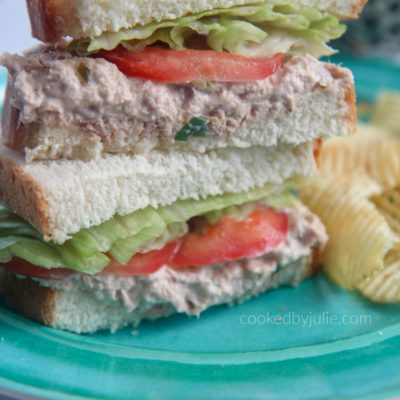 tuna salad sanwiches stacked on a blue plate with potato chips on the side