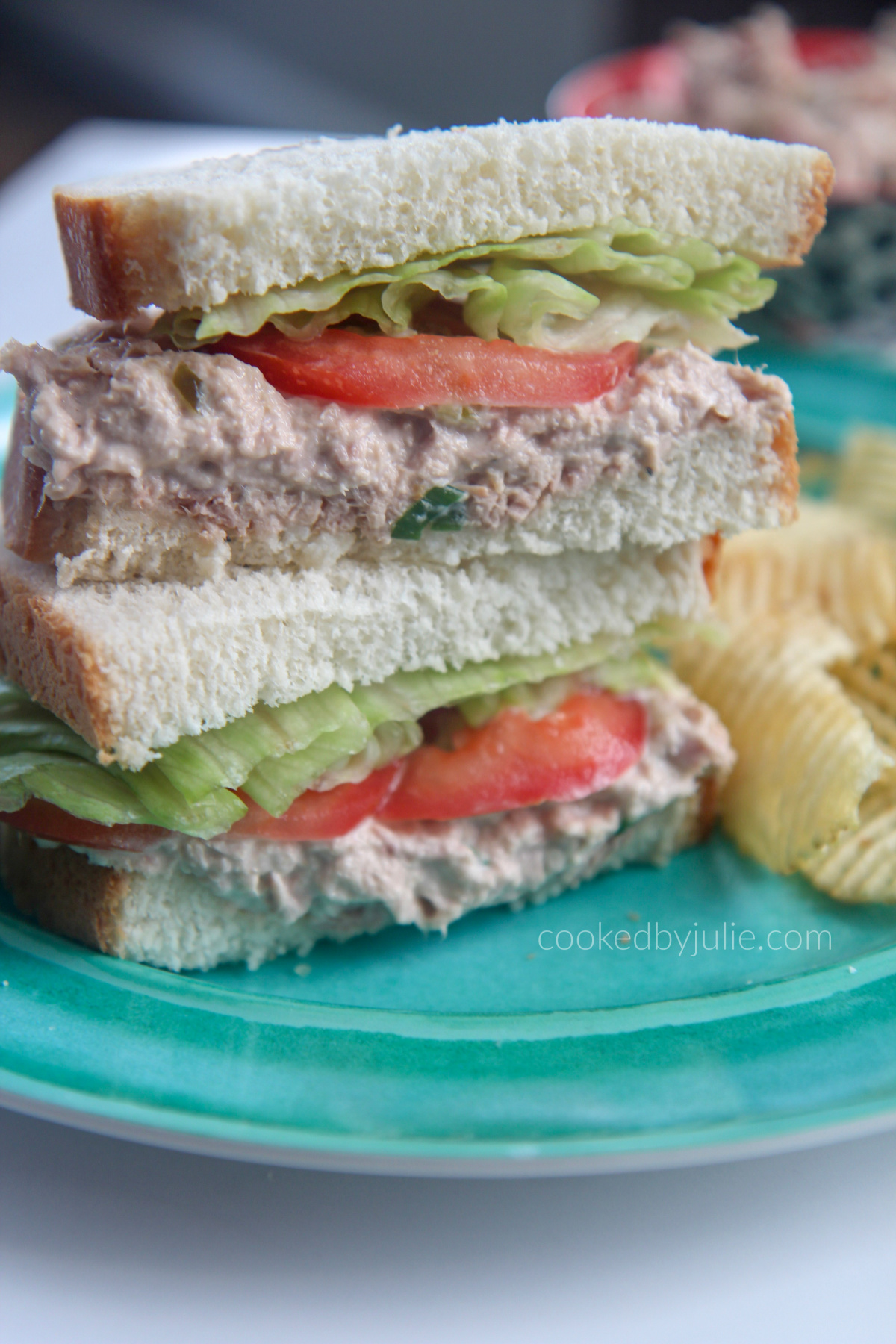 tuna salad sanwiches stacked on a blue plate with potato chips on the side 