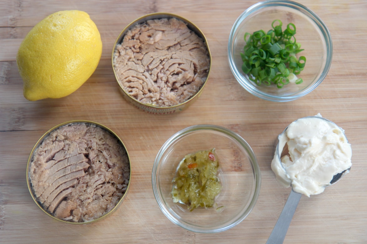 canned tuna, lemon, sweet relish, mayo, and scallions in small bowls on a wooden board