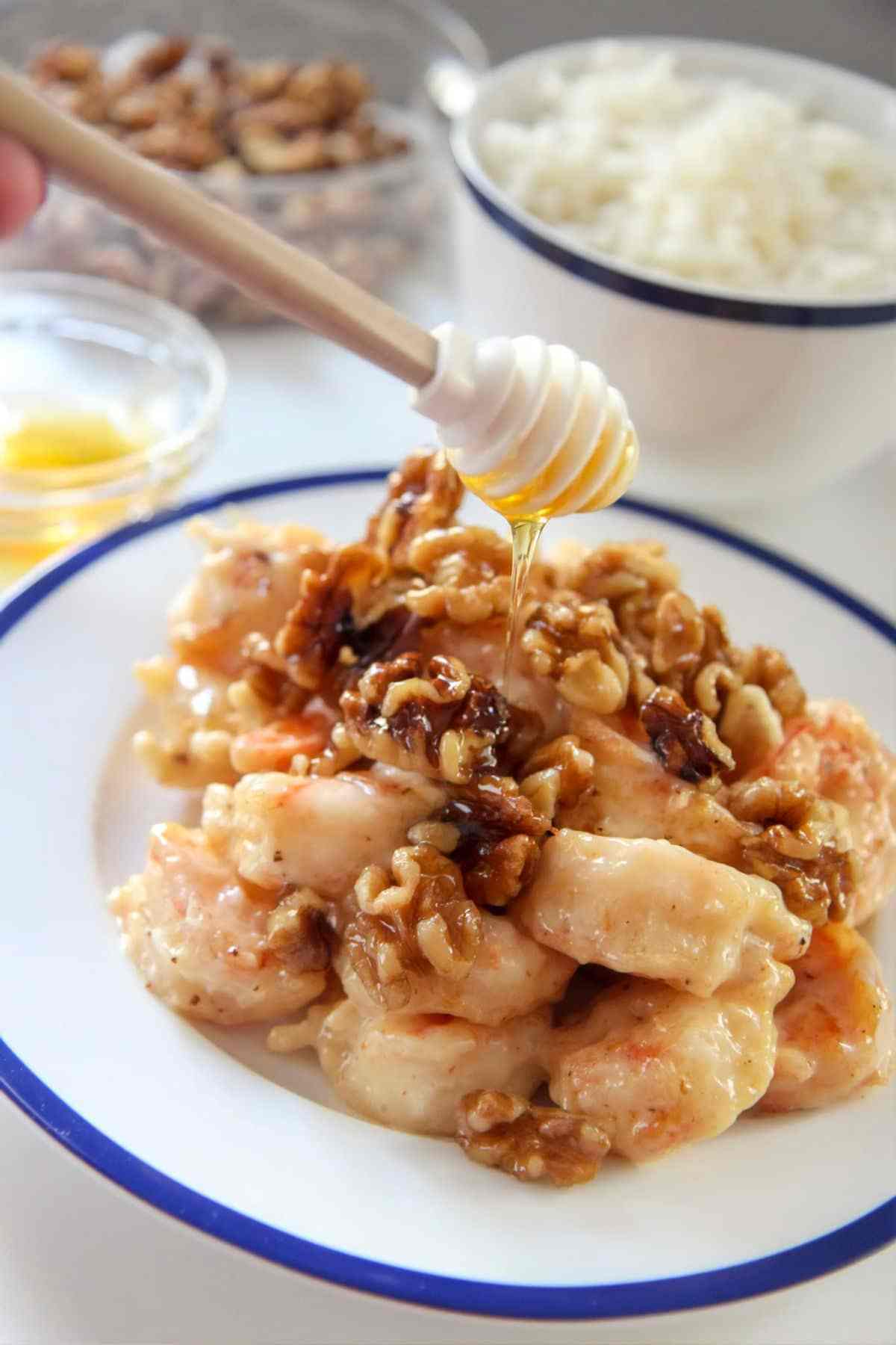 honey walnut shrimp on a white and blue plate with a honey dipper. 