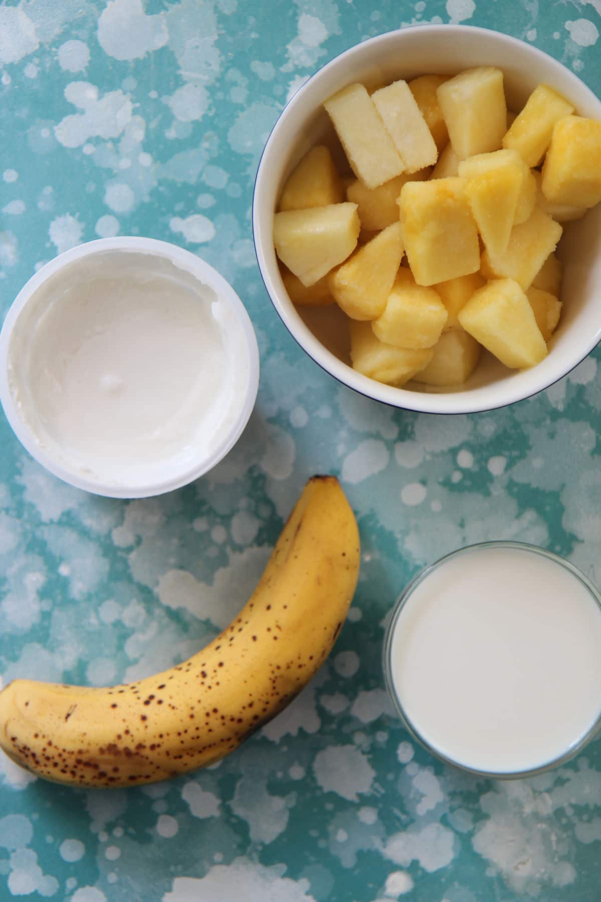 frozen pineapples, milk, yogurt, and banana on a blue and white board.