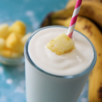 pineapple banana smoothie in a glass with a pink a white straw and fruit on top