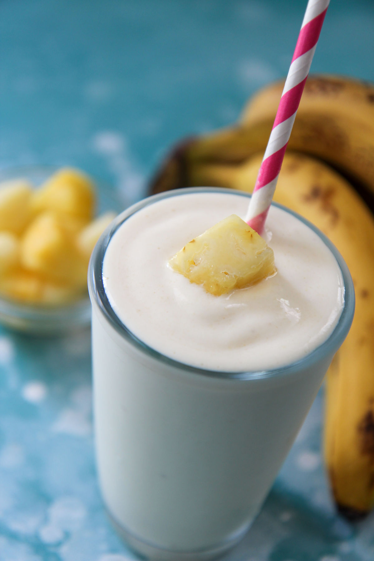 pineapple banana smoothie in a glass with a pink a white straw and fruit on top