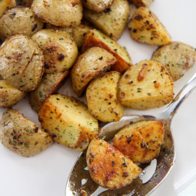 two potatoes on a slotted spoon on a white plate with more potatoes around the spoon.